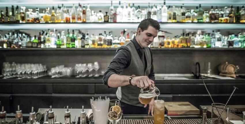 Barman en cravate versant un cocktail derrière le bar.