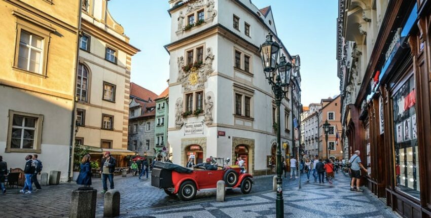 Scène de rue historique, bâtiments, piétons, voiture vintage rouge.
