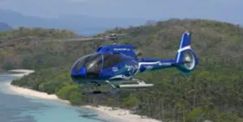 Hélicoptère EC 130 B4 survolant plage et montagnes.